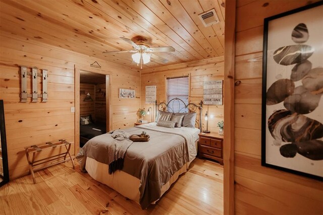 bedroom with wood walls, wooden ceiling, a walk in closet, light hardwood / wood-style flooring, and ceiling fan