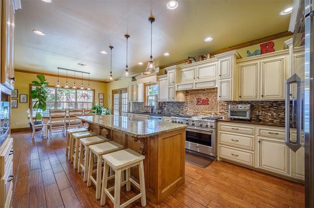 kitchen with light stone countertops, premium appliances, cream cabinets, decorative light fixtures, and a kitchen island