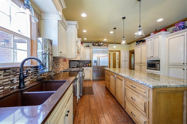 kitchen featuring a large island, sink, built in appliances, hardwood / wood-style floors, and pendant lighting