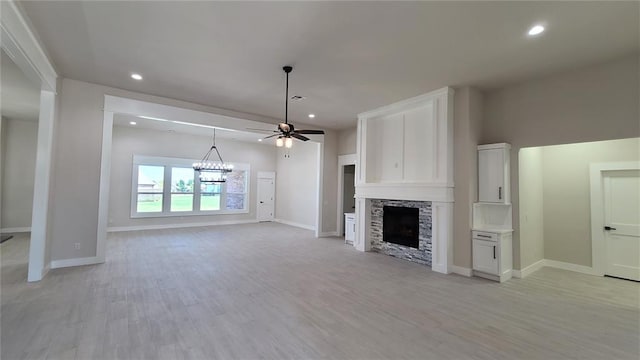 unfurnished living room with ceiling fan with notable chandelier, light hardwood / wood-style floors, and a stone fireplace