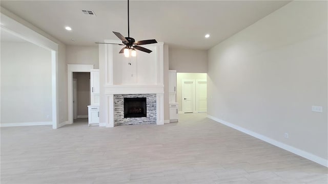 unfurnished living room featuring a fireplace, light wood-type flooring, a towering ceiling, and ceiling fan