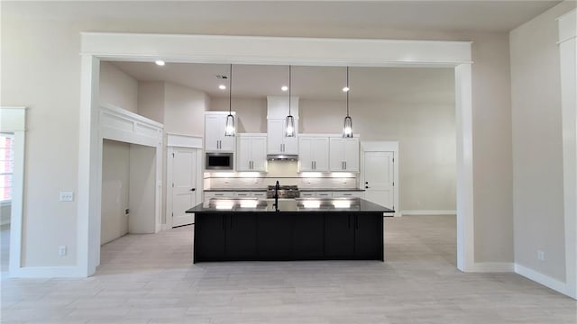 kitchen with stainless steel microwave, sink, decorative light fixtures, a kitchen island with sink, and white cabinets