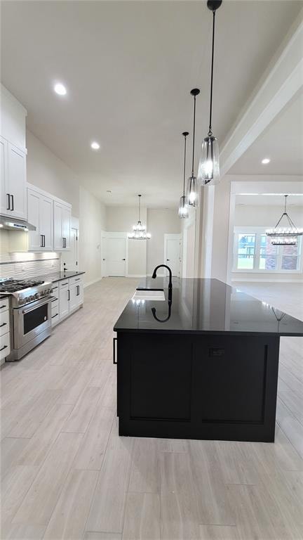 kitchen featuring pendant lighting, sink, high end stove, an island with sink, and white cabinetry