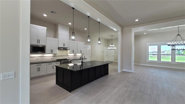 kitchen with pendant lighting, a kitchen island with sink, light wood-type flooring, white cabinetry, and stainless steel appliances