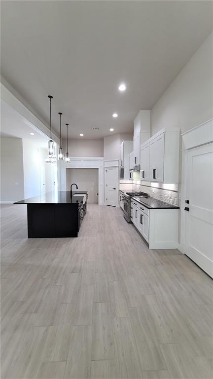 kitchen featuring a kitchen island with sink, pendant lighting, light hardwood / wood-style flooring, white cabinets, and stainless steel range with gas cooktop