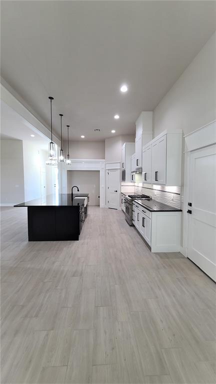 1425 W Harvard Way, Mustang, OK 73064 - kitchen featuring stainless steel stove, an island with sink, white cabinets, recessed lighting, and decorative light fixtures