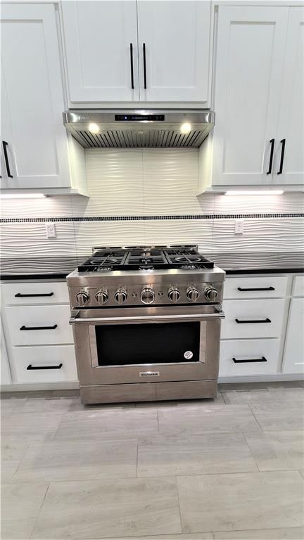 kitchen with backsplash, white cabinetry, high end stainless steel range oven, and extractor fan