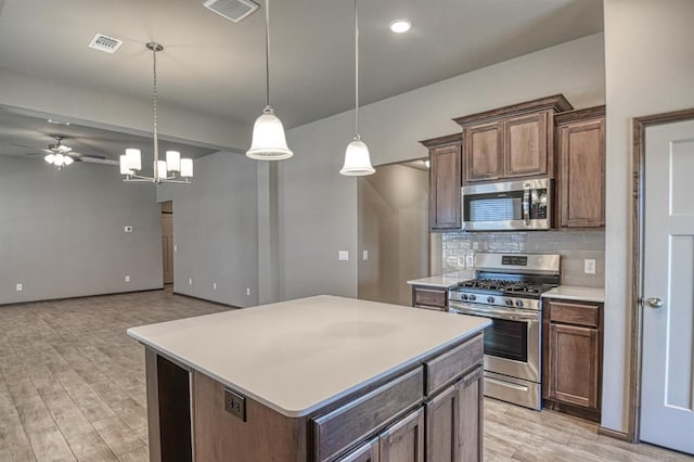 kitchen featuring a center island, hanging light fixtures, decorative backsplash, ceiling fan with notable chandelier, and appliances with stainless steel finishes