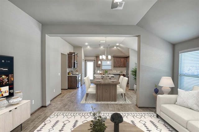 living room with plenty of natural light, a chandelier, vaulted ceiling, and light wood-type flooring