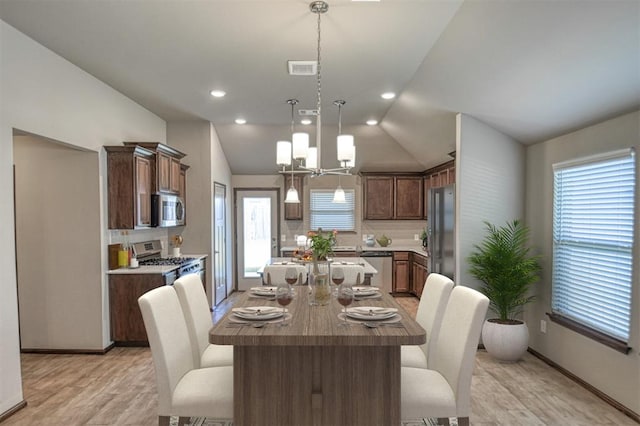 dining space with light hardwood / wood-style flooring, vaulted ceiling, and a notable chandelier