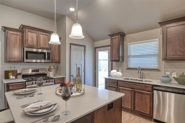 kitchen featuring decorative backsplash, stainless steel appliances, vaulted ceiling, sink, and pendant lighting