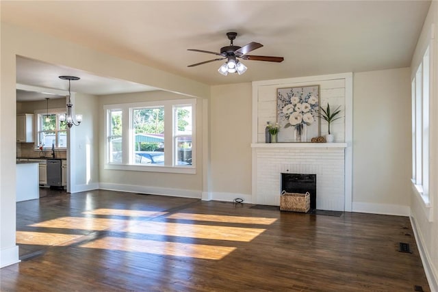 unfurnished living room featuring dark hardwood / wood-style floors, sink, ceiling fan with notable chandelier, and a brick fireplace