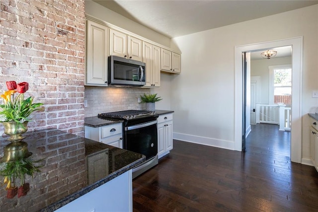 kitchen with decorative backsplash, dark hardwood / wood-style flooring, dark stone counters, and appliances with stainless steel finishes