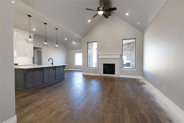 unfurnished living room with ceiling fan, a fireplace, sink, high vaulted ceiling, and dark hardwood / wood-style flooring