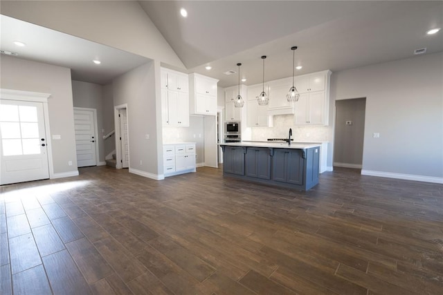 kitchen featuring white cabinetry, an island with sink, decorative light fixtures, high vaulted ceiling, and sink