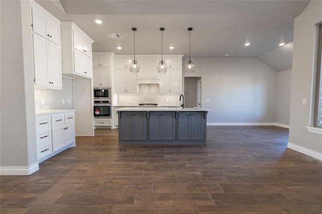 kitchen featuring hanging light fixtures, white cabinets, vaulted ceiling, and a center island with sink