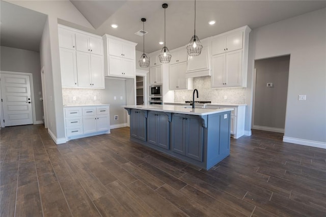 kitchen featuring vaulted ceiling, white cabinetry, pendant lighting, and a center island with sink