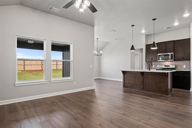 kitchen with lofted ceiling, a kitchen island with sink, hanging light fixtures, dark hardwood / wood-style floors, and appliances with stainless steel finishes