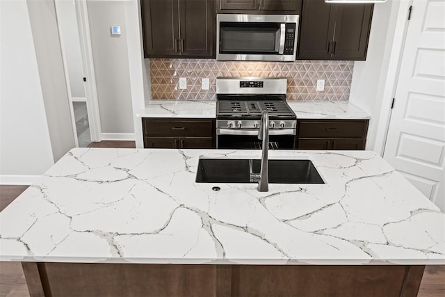 kitchen with backsplash, light stone counters, dark brown cabinets, and stainless steel appliances