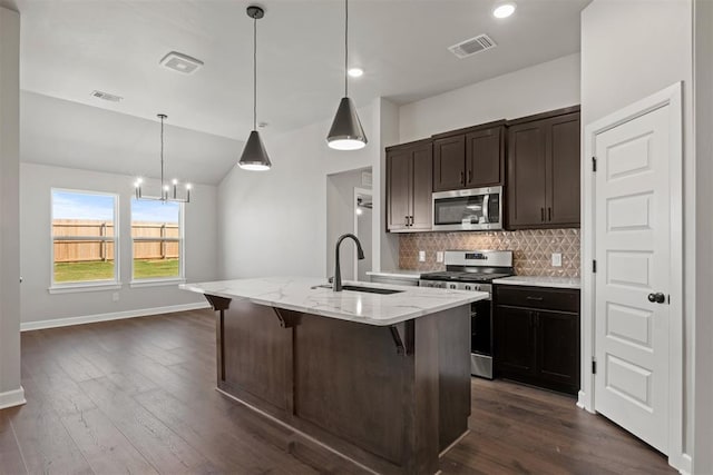 kitchen with sink, dark hardwood / wood-style floors, an island with sink, decorative light fixtures, and appliances with stainless steel finishes