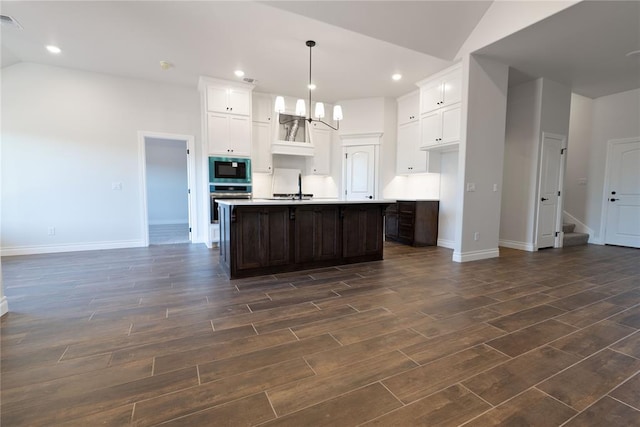 kitchen featuring built in microwave, sink, oven, decorative light fixtures, and a kitchen island with sink