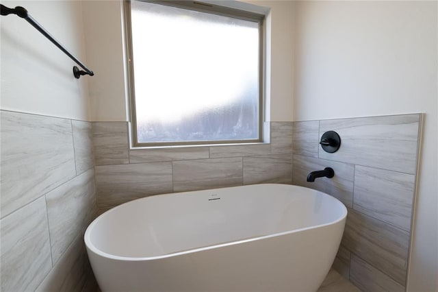 bathroom with a bathing tub, plenty of natural light, and tile walls