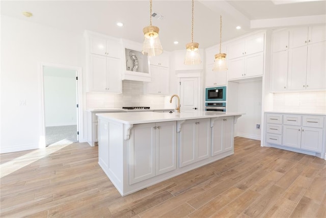 kitchen featuring decorative light fixtures, built in microwave, white cabinets, oven, and a kitchen island with sink