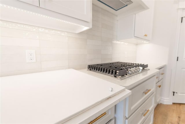 kitchen featuring light hardwood / wood-style flooring, white cabinetry, tasteful backsplash, stainless steel gas cooktop, and exhaust hood