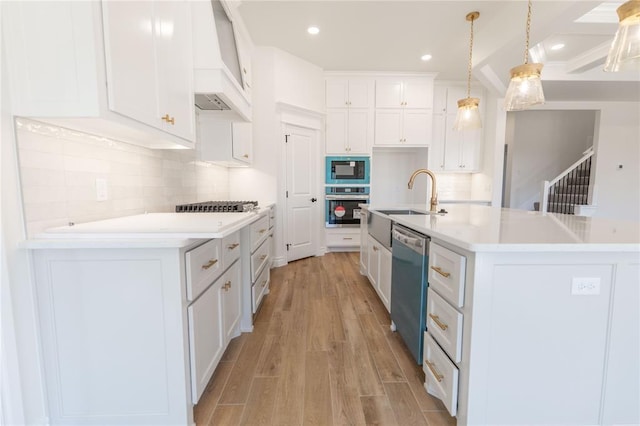 kitchen featuring custom exhaust hood, white cabinetry, hanging light fixtures, stainless steel appliances, and a kitchen island with sink