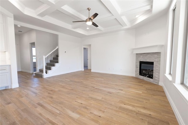 unfurnished living room with a stone fireplace, light hardwood / wood-style flooring, ceiling fan, and a towering ceiling