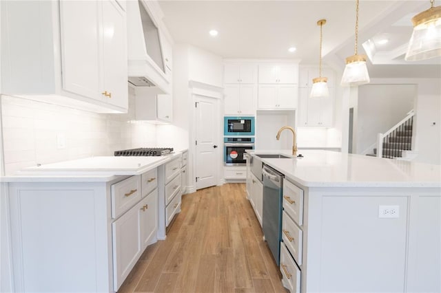 kitchen with custom exhaust hood, stainless steel appliances, light wood-style floors, white cabinetry, and a sink