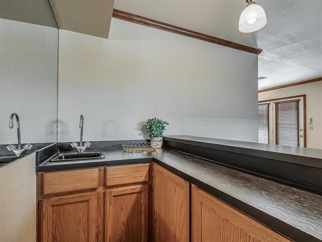 kitchen featuring a textured ceiling, decorative light fixtures, crown molding, and sink