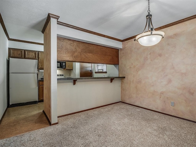 kitchen featuring kitchen peninsula, ornamental molding, decorative light fixtures, white fridge, and a breakfast bar area