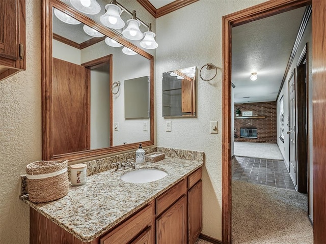 bathroom featuring a textured ceiling, vanity, crown molding, and a brick fireplace