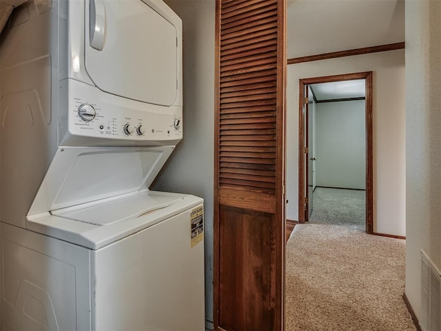 clothes washing area with stacked washer / drying machine, carpet floors, and crown molding