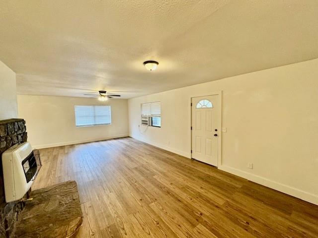 unfurnished living room featuring a textured ceiling, heating unit, ceiling fan, light hardwood / wood-style flooring, and a stone fireplace