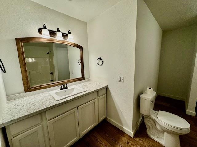 bathroom with wood-type flooring, vanity, toilet, and walk in shower