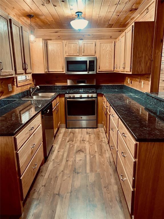 kitchen with sink, wooden ceiling, hanging light fixtures, stainless steel appliances, and light wood-type flooring