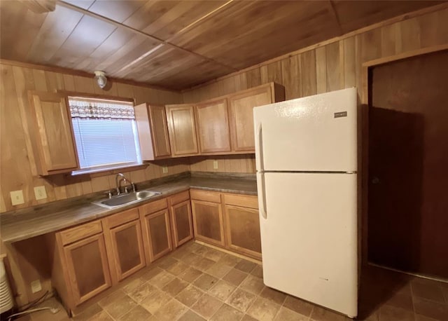 kitchen featuring white refrigerator, wood ceiling, wooden walls, and sink