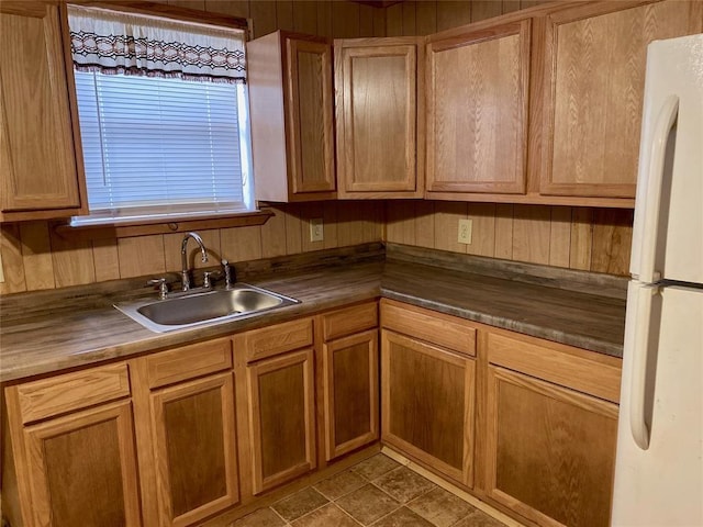 kitchen featuring white fridge, tile patterned floors, wooden walls, and sink