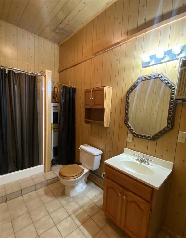 bathroom with vanity, wooden walls, wooden ceiling, tile patterned flooring, and toilet