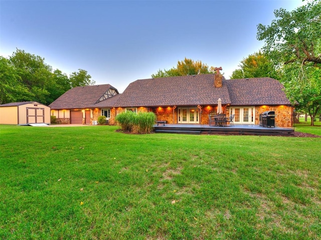 rear view of property with a lawn, french doors, and a storage unit