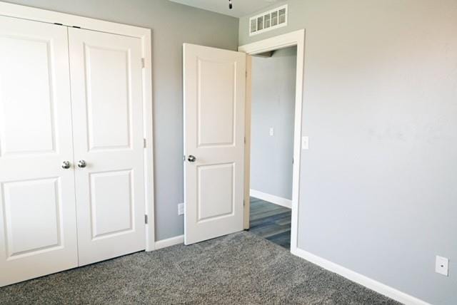 unfurnished bedroom with dark carpet and a closet