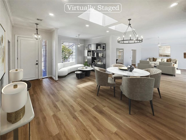 dining space with wood-type flooring, ceiling fan with notable chandelier, and crown molding