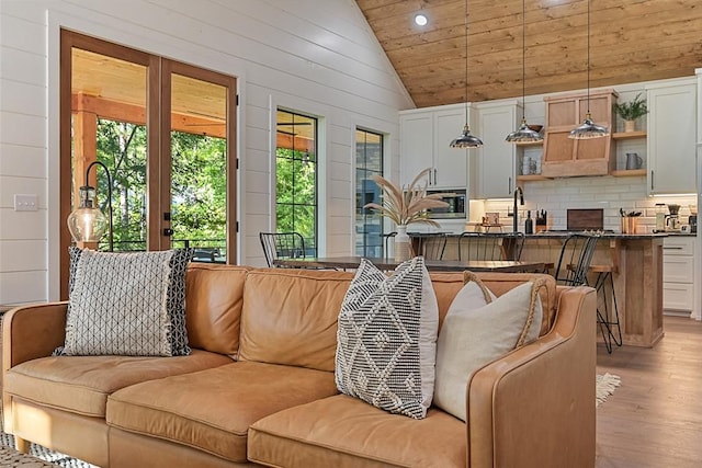 living room with wood walls, light hardwood / wood-style floors, and high vaulted ceiling