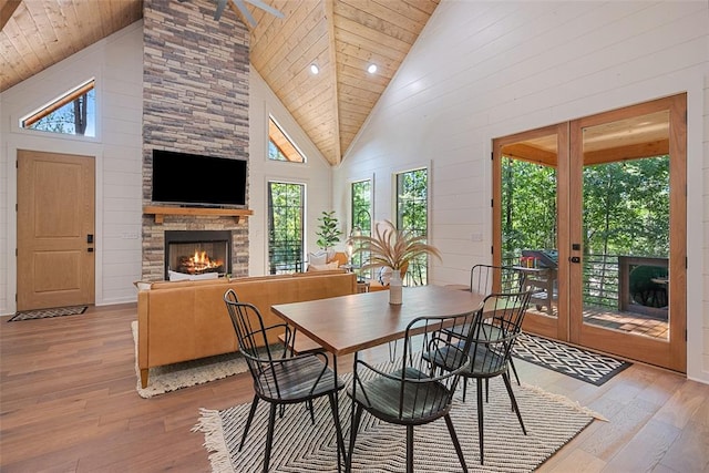 dining room with french doors, light hardwood / wood-style flooring, high vaulted ceiling, and a stone fireplace