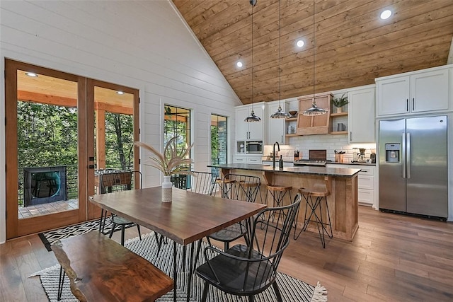 dining area featuring sink, wooden ceiling, light hardwood / wood-style flooring, high vaulted ceiling, and wood walls