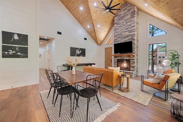 dining area with wooden ceiling, hardwood / wood-style flooring, high vaulted ceiling, and a stone fireplace