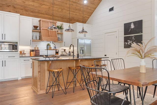 kitchen featuring decorative light fixtures, stainless steel appliances, white cabinetry, and an island with sink