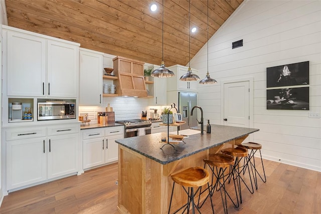 kitchen with high vaulted ceiling, stainless steel appliances, white cabinetry, and a kitchen island with sink